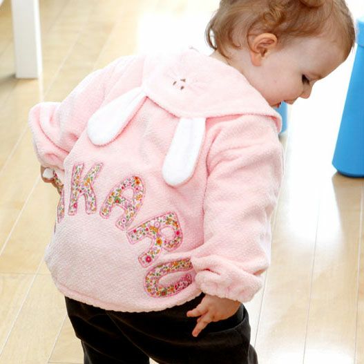 ピンク色のタオル素材ジャンパーを着た幼い女の子が床に立ってふりむいている姿