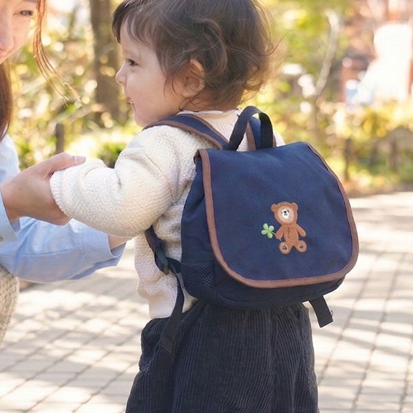 くまの刺しゅう入りリュックを背負って保護者と歩く女の子